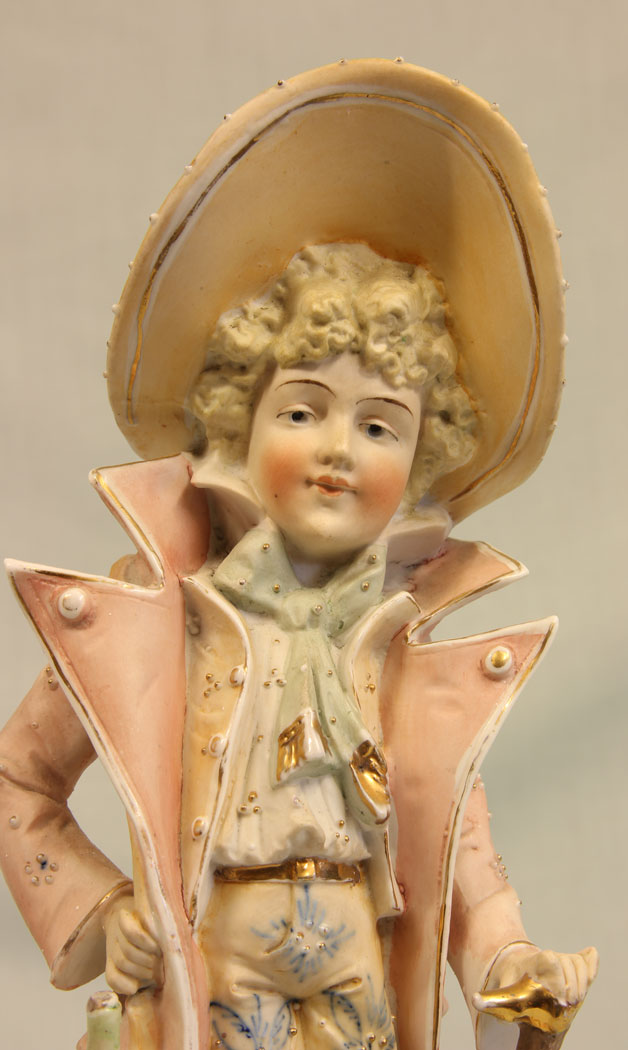 11384r2 Antique Bisque Figurine of Gentleman, Antique Bisque Figurine of Gentleman. This lovely bisque figure of young gentleman is dressed in period clothing and hat all in lovely colours and having hand painted detail with gilt decoration he is holding a bag and a cane. There is a slight chip on the bag see photo. Circa 1900